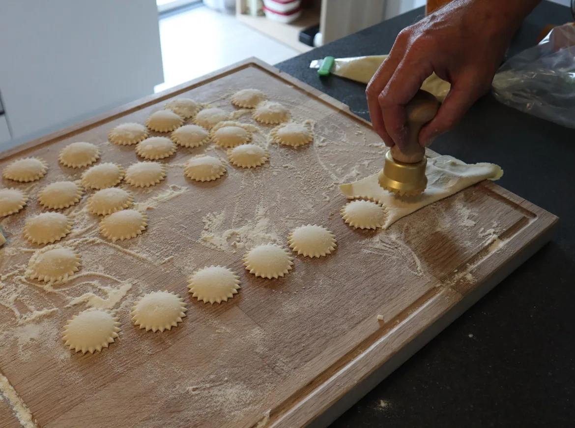 Rows of scalloped ravioli on a floured wooden board beside a stamp cutter