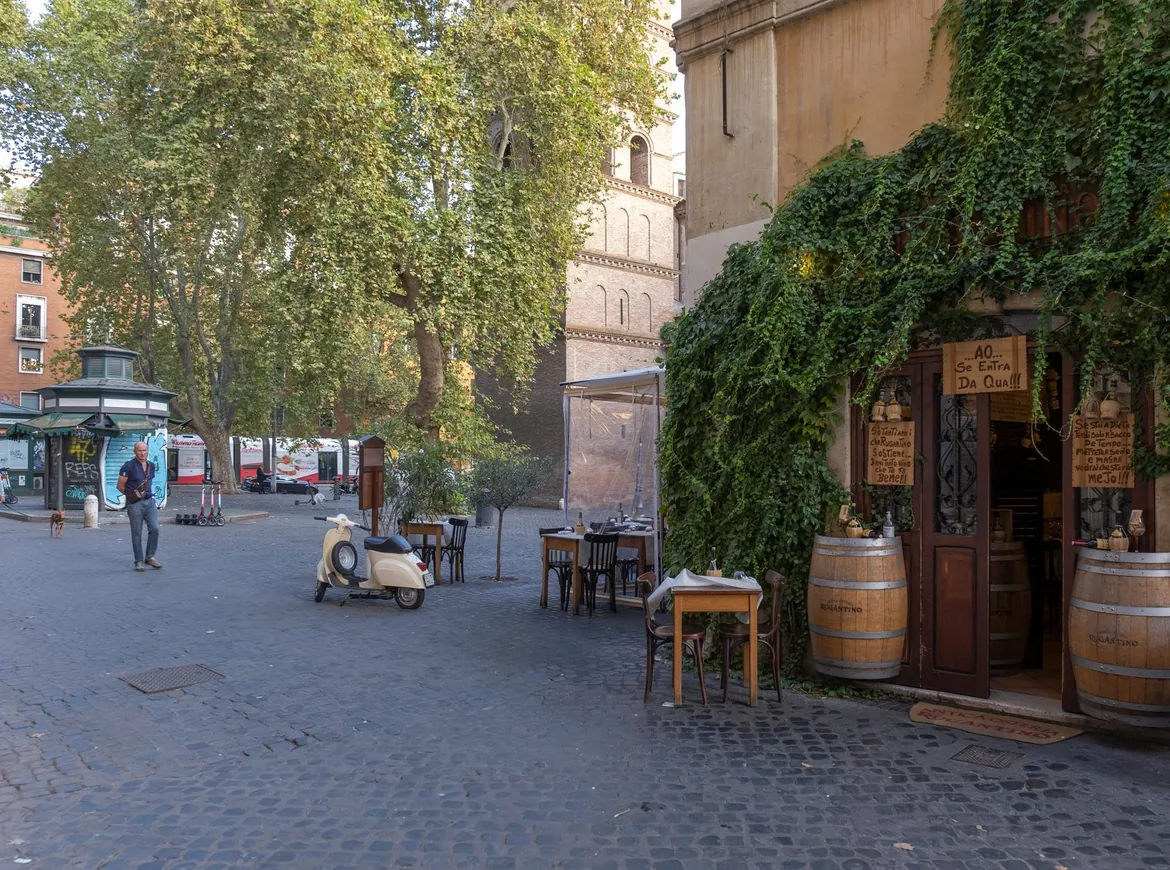 A quiet Roman street with an ivy-covered trattoria, outdoor tables and a parked scooter